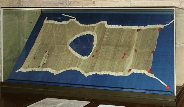 A cilice of coarse woven hair, laid flat in a museum case on blue cloth, marked with red wax seals.